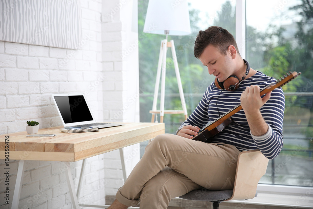 Young composer sitting at a desk with a laptop in light room Young composer sitting at a desk with a laptop in light room