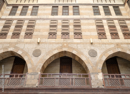 Low angle view of the facade of caravansary (Wikala) of al-Ghuri with vaulted arcades, wooden balustrades, and windows covered by interleaved wooden grids (mashrabiyya), Medieval Cairo, Egypt photo