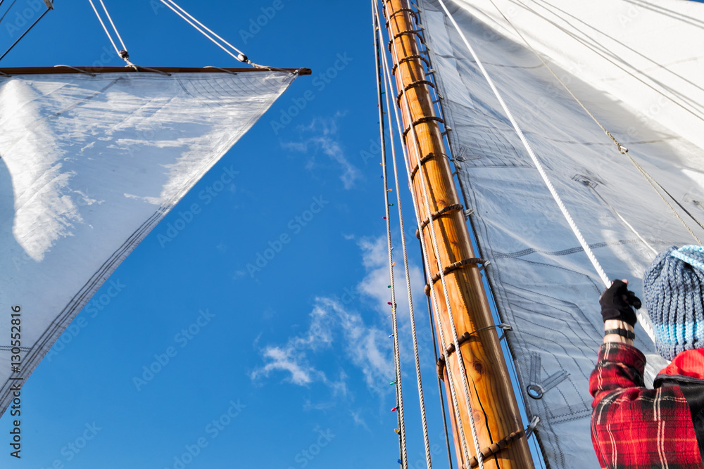 Obraz premium Sailboat crew raising white canvas sail. View looking up
