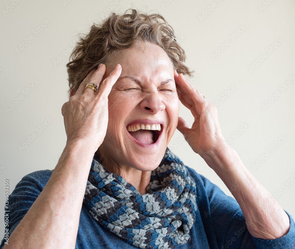 Head and shoulders view of older woman in blue clothing with hands on head screaming (selective focus) Head and shoulders view of older woman in blue clothing with hands on head screaming (selective focus)