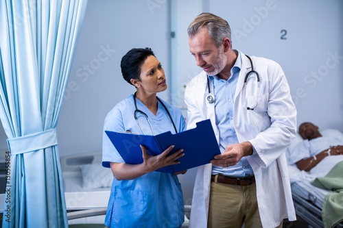 Doctor and nurse having discussion on file in ward