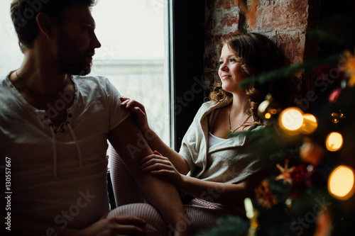 Happy couple of lovers in pajamas sit on the windowsill. Christmas atmosphere.