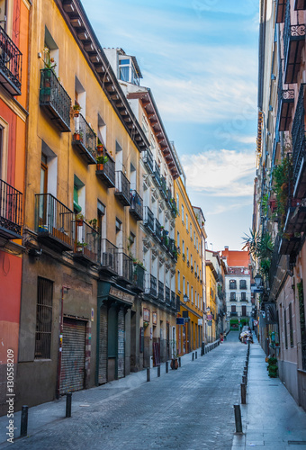 Quiet alley street scene  in Madrid  Spain.  Two women and a child at the far end  crossing the lane.  Colourful tall apartment buildings walls lined the street along with narrow sidewalks.