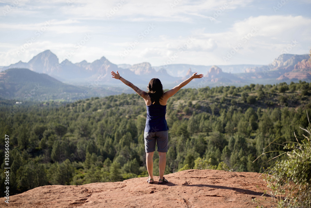 Rear view of hiker with arms outstretched standing on cliff against forest Rear view of hiker with arms outstretched standing on cliff against forest
