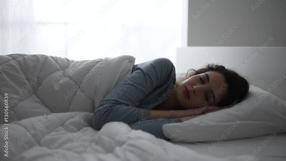 Young beautiful woman waking up at dawn in her bed, she is smiling and well rested Young beautiful woman waking up at dawn in her bed, she is smiling and well rested