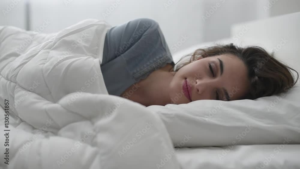 Young attractive woman waking up in her bed in the morning, she is smiling and opening her eyes Young attractive woman waking up in her bed in the morning, she is smiling and opening her eyes