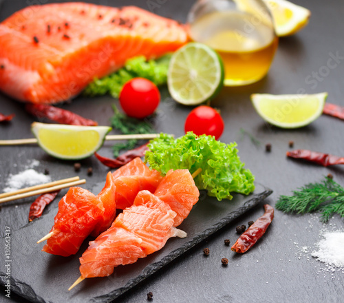 Raw salmon skewers on a stone plate. tomatoes, lime and lettuce for cooking.