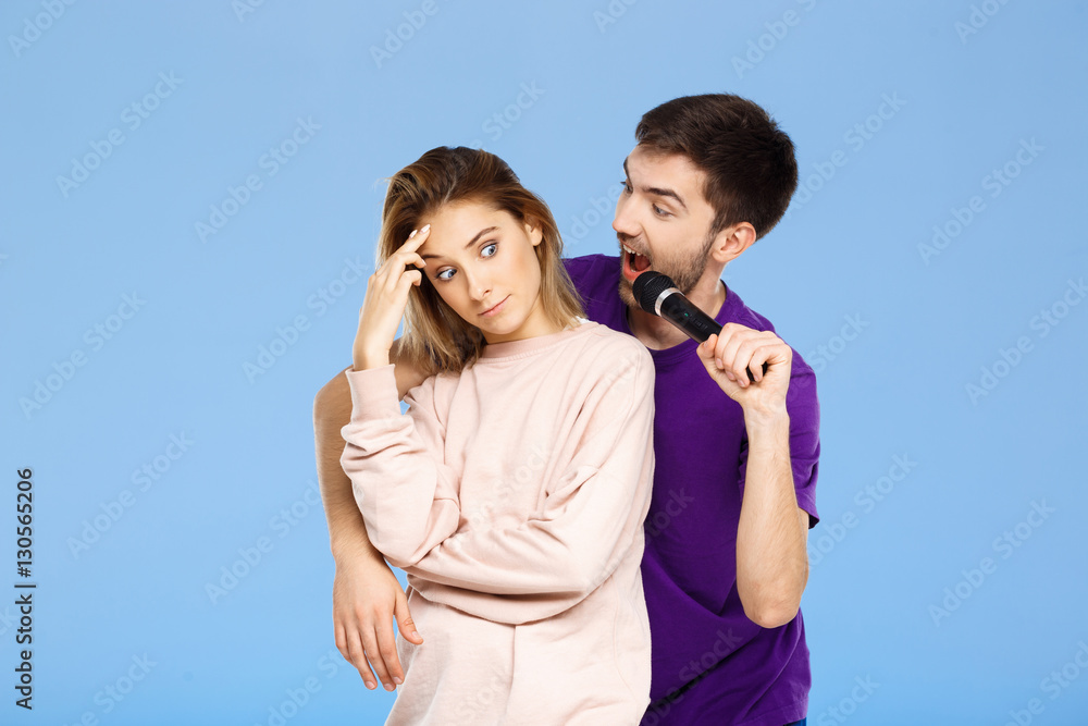 Beautiful couple over blue background. Man singing in microphone girl didpleased. Beautiful couple over blue background. Man singing in microphone girl didpleased.