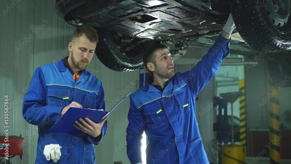 Young workshop employees working together underneath a lifted car Young workshop employees working together underneath a lifted car