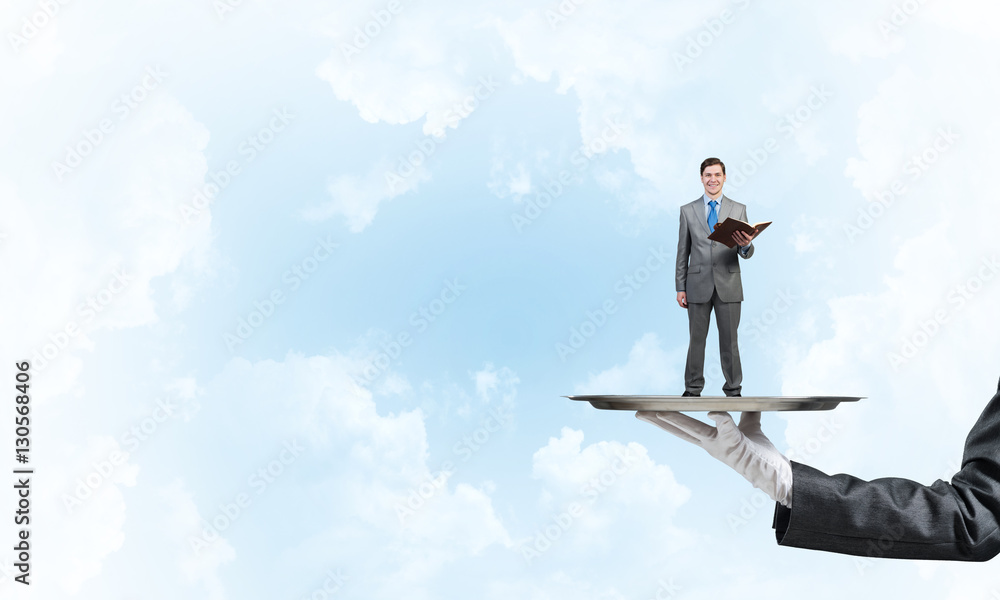 Businessman on metal tray with red book in hands against blue sky background Businessman on metal tray with red book in hands against blue sky background