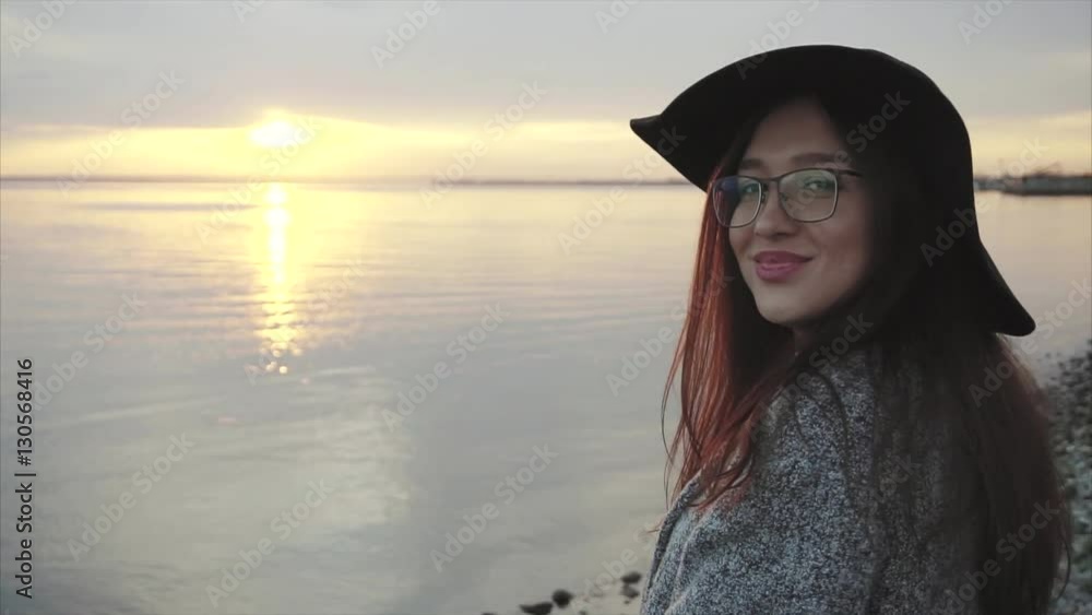 Young pretty smiling woman in black hat and glasses near the sea at sunset HD Young pretty smiling woman in black hat and glasses near the sea at sunset HD