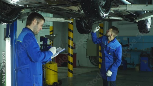 two Mechanic checking on a car engine and taking notes