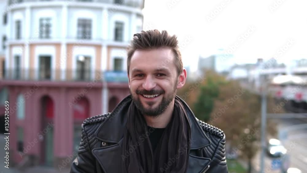 A handsome brutal man with a beard looking into camera, winks, smiling nicely in the city. Slow mo A handsome brutal man with a beard looking into camera, winks, smiling nicely in the city. Slow mo