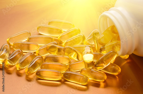 Fish oil capsules with omega 3 and vitamin D in a plastic bottle on a shiny texture with sun beams, healthy diet concept