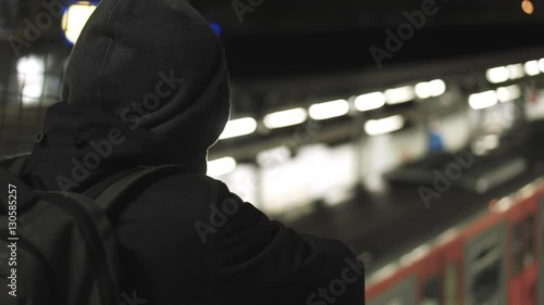 MIllenial youth in hoodie at the train station at night, slomo 100p.A hooded young man is waiting for the train or walking along the platform with or witout his hoodie on, at night.100fps slow motion. photo