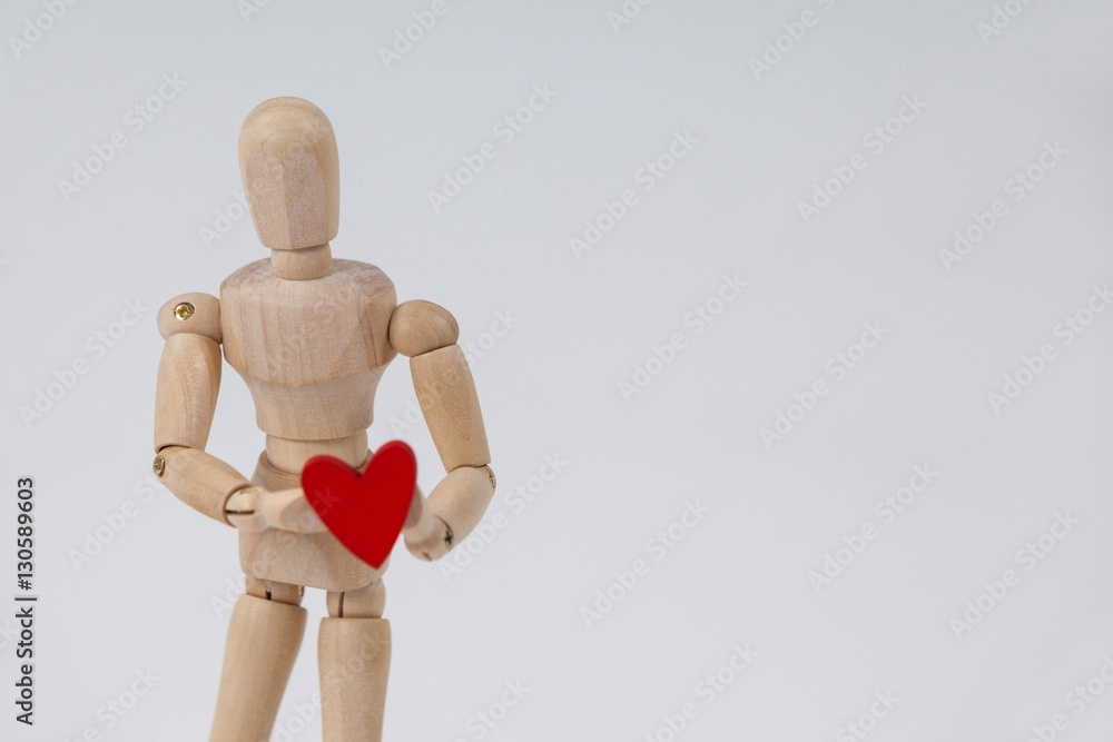 Wooden figurine standing and holding a red heart in front Wooden figurine standing and holding a red heart in front