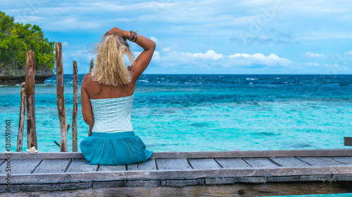 Girl Sitting on Wooden Pier of an Homestay looking into blue ocean, Gam Island, West Papuan, Raja Ampat, Indonesia photo