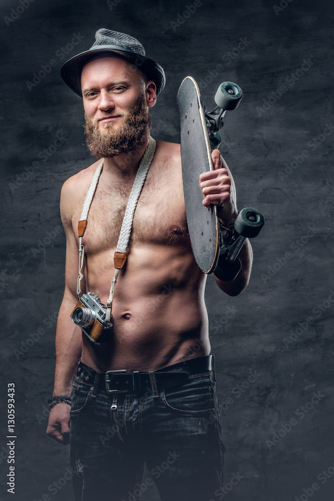 The shirtless bearded male holds skateboard. The shirtless bearded male holds skateboard.