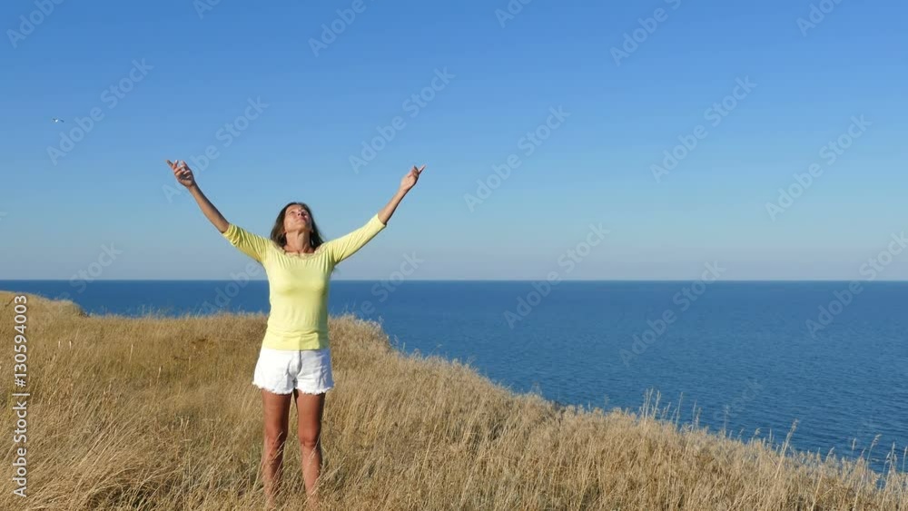 4K. Adult Woman in yellow blouse lifts hands against sea 4K. Adult Woman in yellow blouse lifts hands against sea