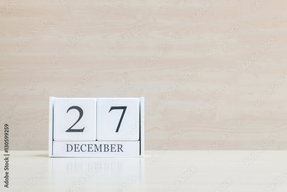 Closeup surface white wooden calendar with black 27 december word on blurred brown wood desk and wood wall textured background with copy space , selective focus at the calendar Closeup surface white wooden calendar with black 27 december word on blurred brown wood desk and wood wall textured background with copy space , selective focus at the calendar