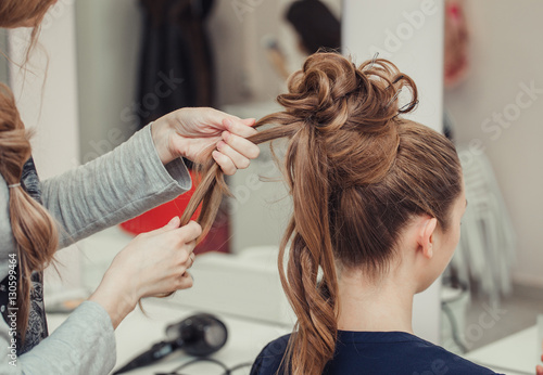 High Hairstyle creating process in hairdresser salon with elegant bun. Blonde and red hairs