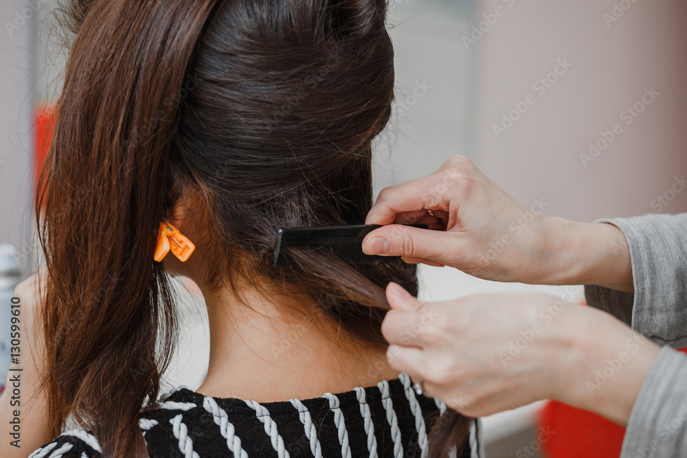 Fototapeta premium professional hairdresser doing a hairstyle to her client with healthy shiny brunette hair in the beauty salon, using comb and barrette
