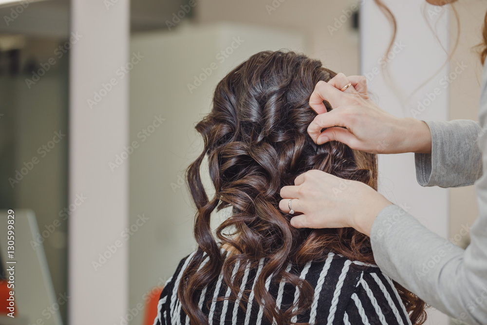 Naklejka premium Close up of hands of professional hairdresser at beauty salon, curling female hair