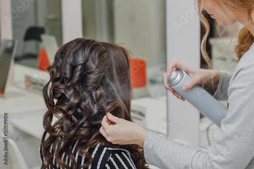 Stylist curling hair and making wedding hairstyle for brown haired woman.