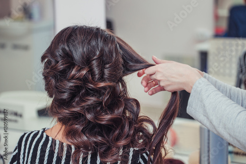 Stylist curling hair and making wedding hairstyle for brown haired woman.