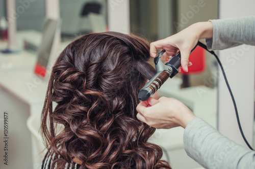 Hairdresser doing wrap curling brunette hair in a beauty salon with iron
