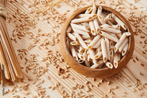 Uncooked whole wheat pasta in wooden bowl surrounded by wheat photo