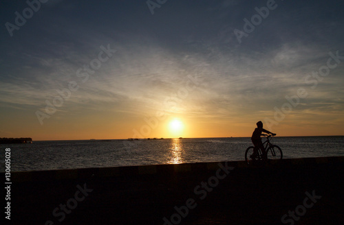 Child with bicycle silhouette in front of the sea at sunset