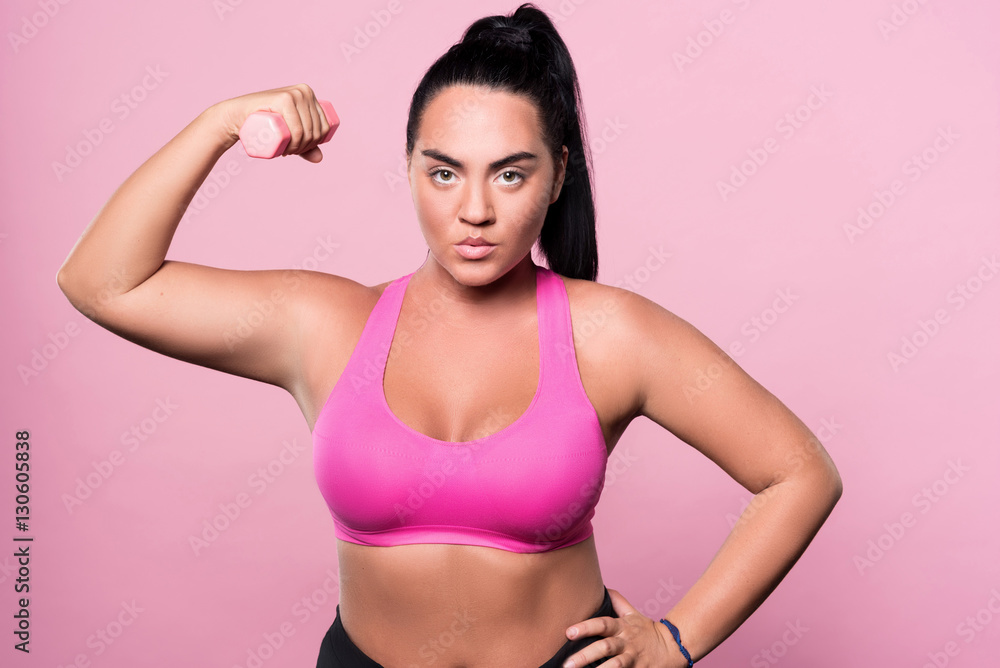 Obraz premium Pretty plump woman posing with small dumbbell
