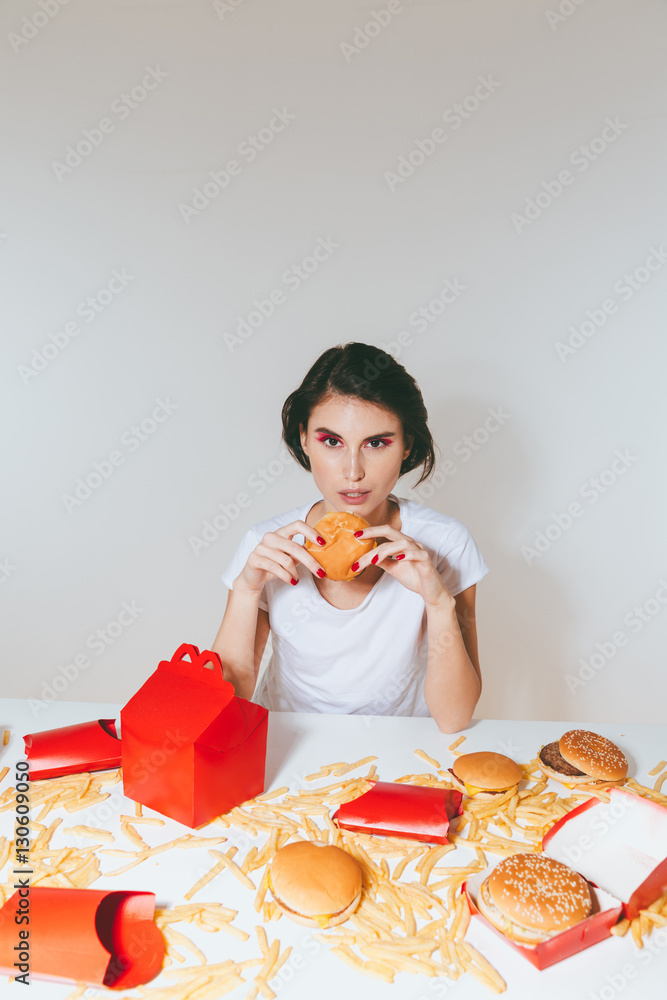 Charming woman eating hamburger from red box at the table Charming woman eating hamburger from red box at the table