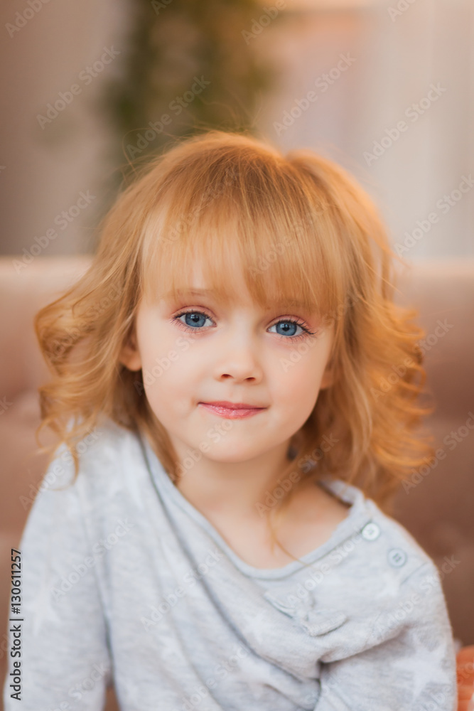 Portrait of beautiful blonde little girl on the couch. A girl in a gray jacket and a fluffy skirt Portrait of beautiful blonde little girl on the couch. A girl in a gray jacket and a fluffy skirt