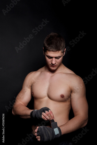 Sports boxer man pulls on the hand wrist wraps. Caucasian male model isolated on dark background. © nazarets