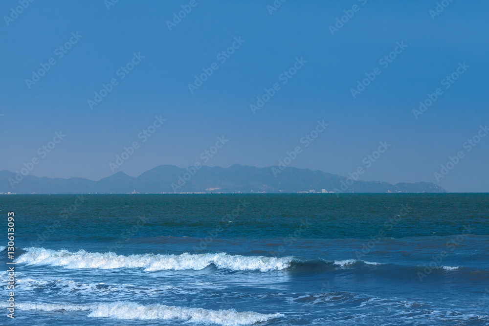 Seascape with surf in bay with port city in mountains