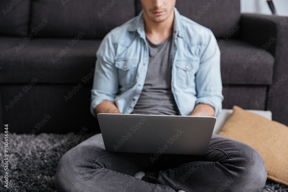 Pensive man working with laptop computer while sitting on carpet Pensive man working with laptop computer while sitting on carpet