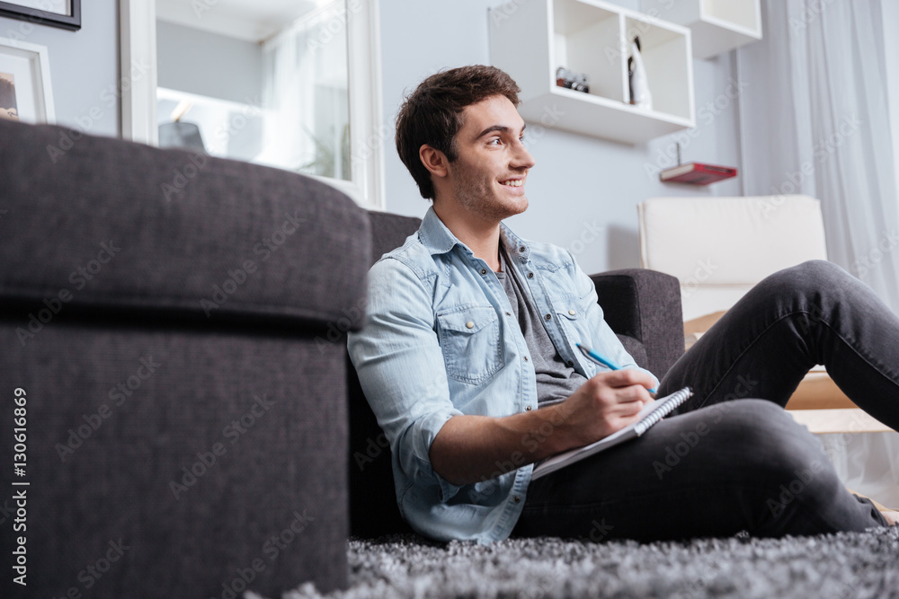 Man making notes in copybook while sitting on the carpet Man making notes in copybook while sitting on the carpet