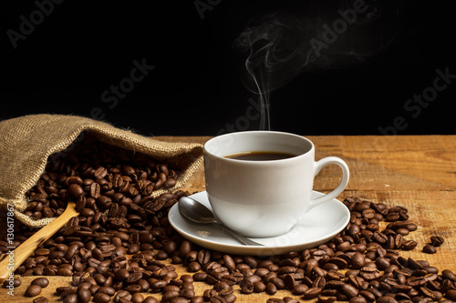 Taza de café con humo y granos de café con bolsa de arpillera sobre mesa de madera rústica de la cocina sobre una tabla de madera rústica y fondo negro. Vista de frente. Copy space