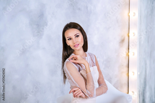 Young Brunette woman with straight and silky hair sitting in front of mirror on grey background looking on camera