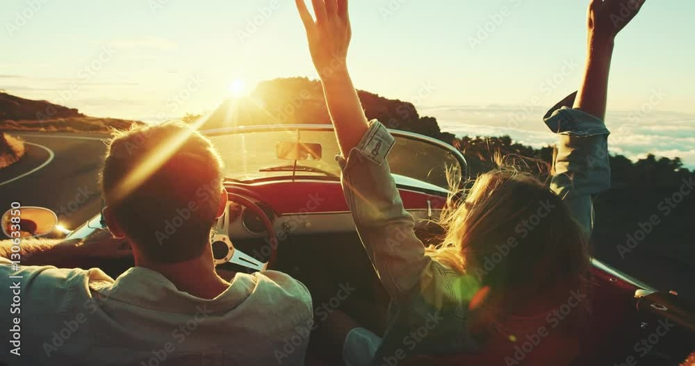 Happy couple driving on country road into the sunset in classic vintage sports car