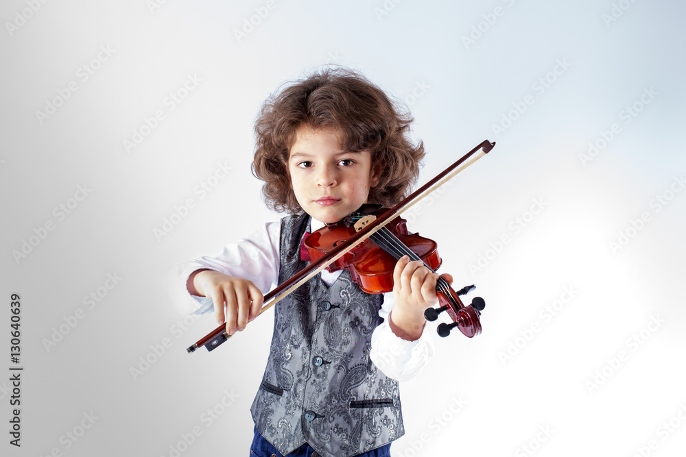 Curly cute violinist waistcoat in playing the violin and looking at the camera. Gray background. Curly cute violinist waistcoat in playing the violin and looking at the camera. Gray background.