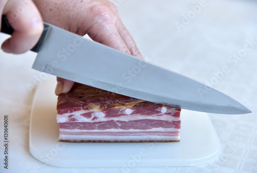 Hands of a woman cutting bacon in slices. Selective focus.
