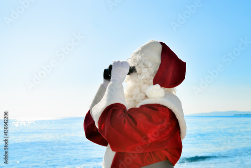 Christmas Vacation - Santa standing on the beach with binoculars, looking for … photo