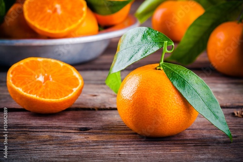 Juicy ripe tangerines with leaves in a bowl on wooden background.