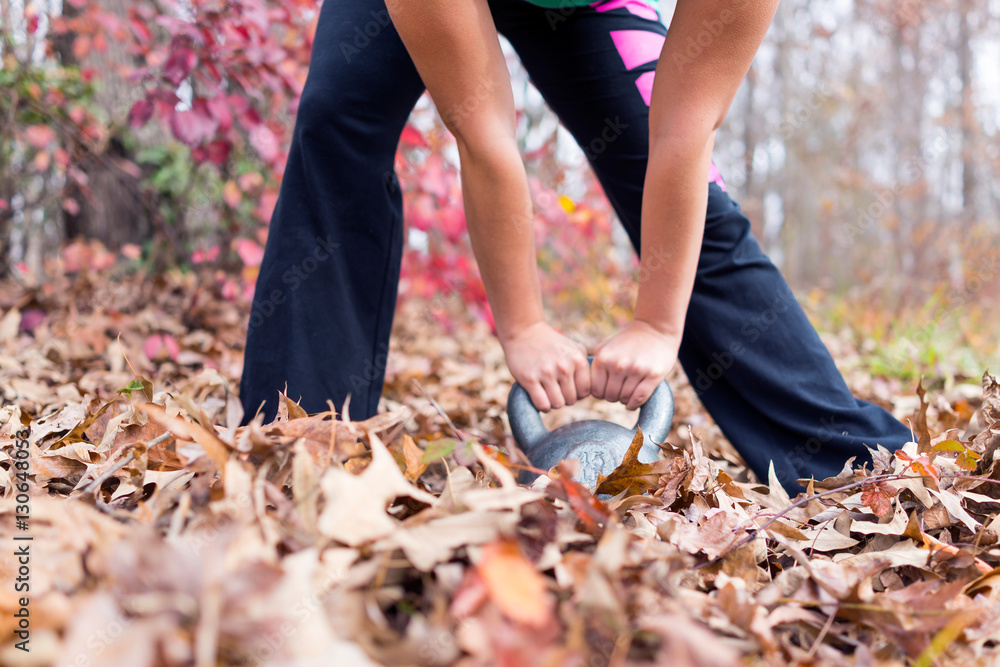 Young fit woman hunched over holding kettlebell in fallen leaves