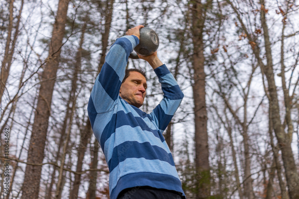 Man lifting heavy kettlebell above head with difficulty