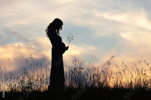 Силуэт беременной женщины на фоне закатного неба