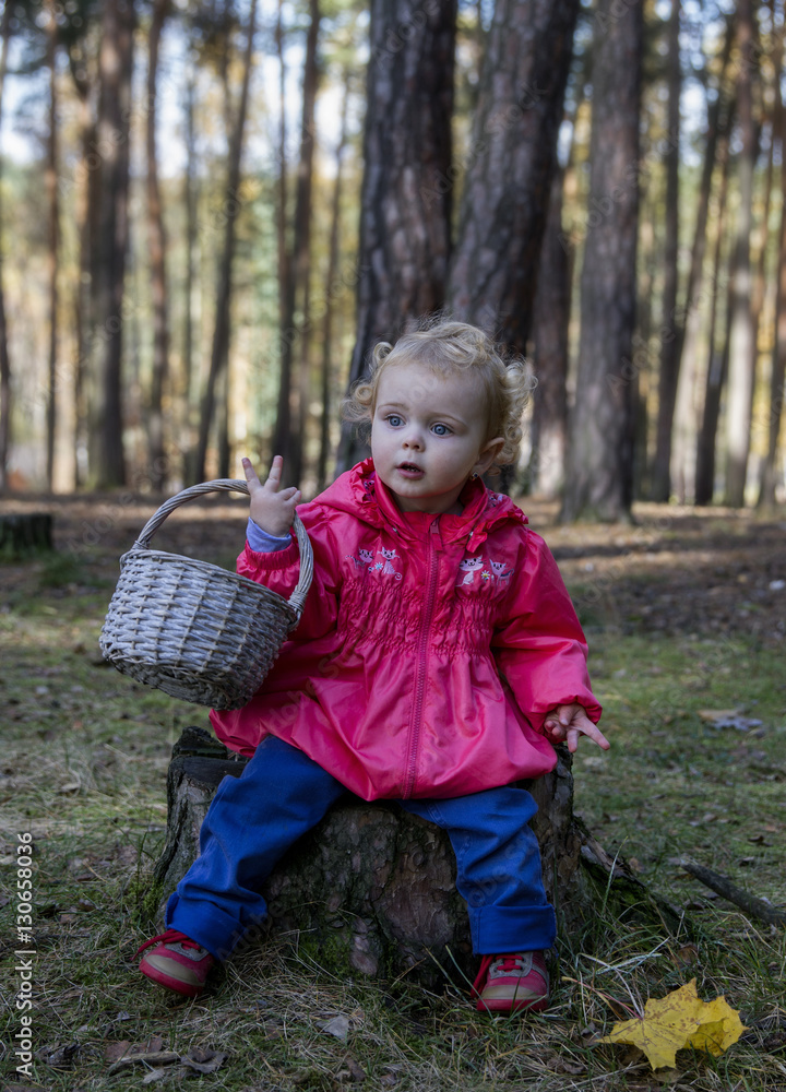 Little girl sitting on a stump in the woods with a basket .